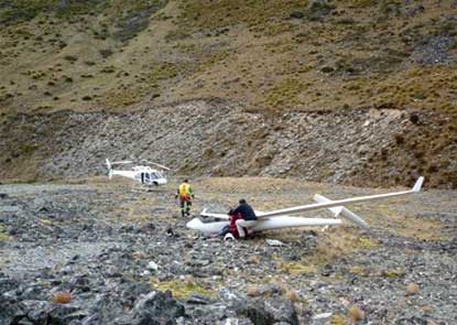 a crashed glider with rescuers nearby and a helicopter landed in the background